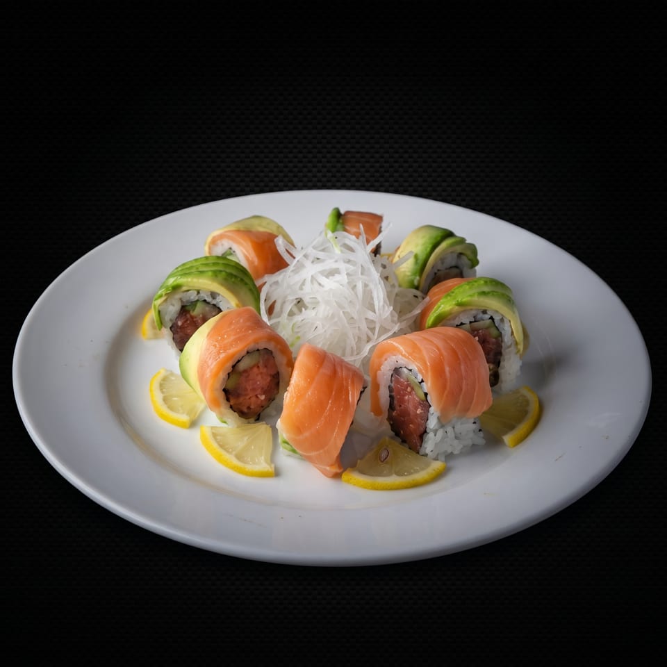 Sushi rolls with salmon and avocado, garnished with lemon and shredded daikon on a white plate.